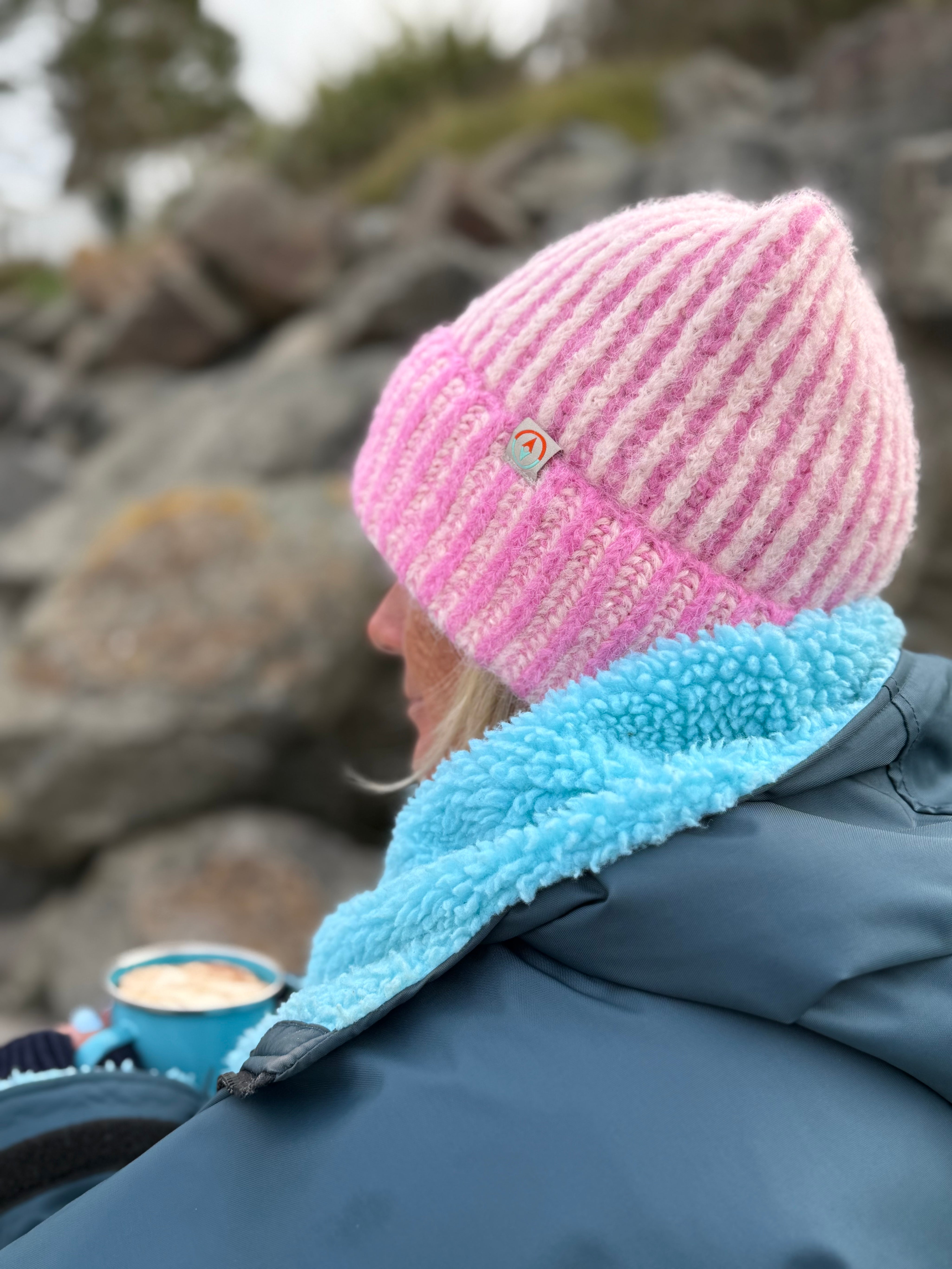 Person wearing a pink and white knit hat with a blue fleece lining, sitting by rocks.