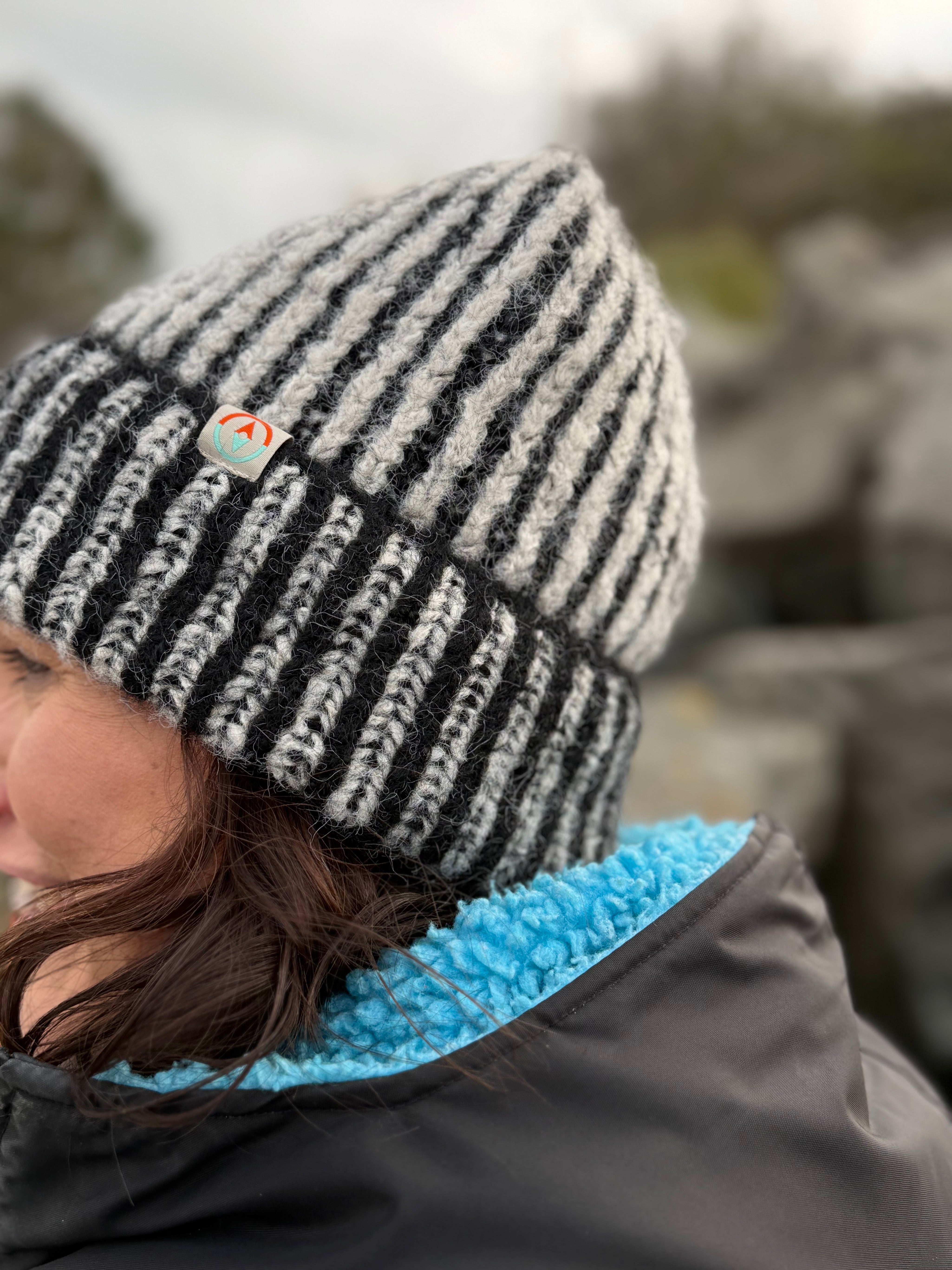 Person wearing a black and white striped beanie with a logo, outdoors.