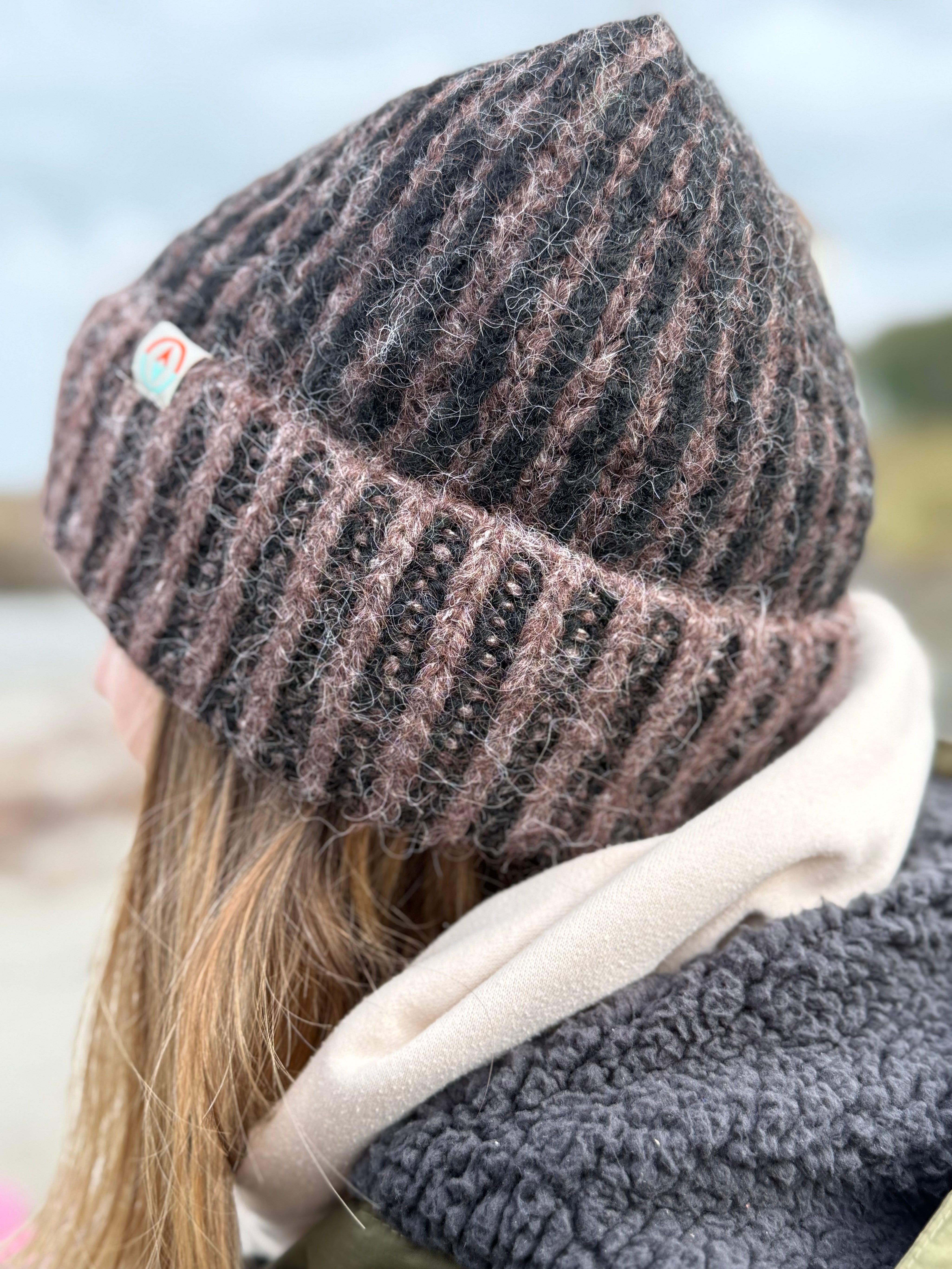 Person wearing a knitted beanie and scarf with a blurred natural background