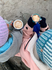 Two people holding hot chocolate on a beach.