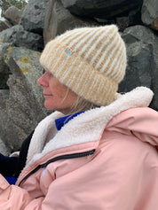 Person wearing a beige knit beanie and pink jacket on a rocky surface