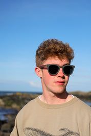 Made with sustainable speckled charcoal wheat straw or coffee residue frame and walnut wood temples, these stylish shades are lightweight, comfortable and eco-friendly with their plastic alternative materials. Fitted with UV400 polarised lenses in a smoke black colour and subtle logo is engraved on the temples. Sunglasses come with a padded pouch and microfibre cleaning cloth.