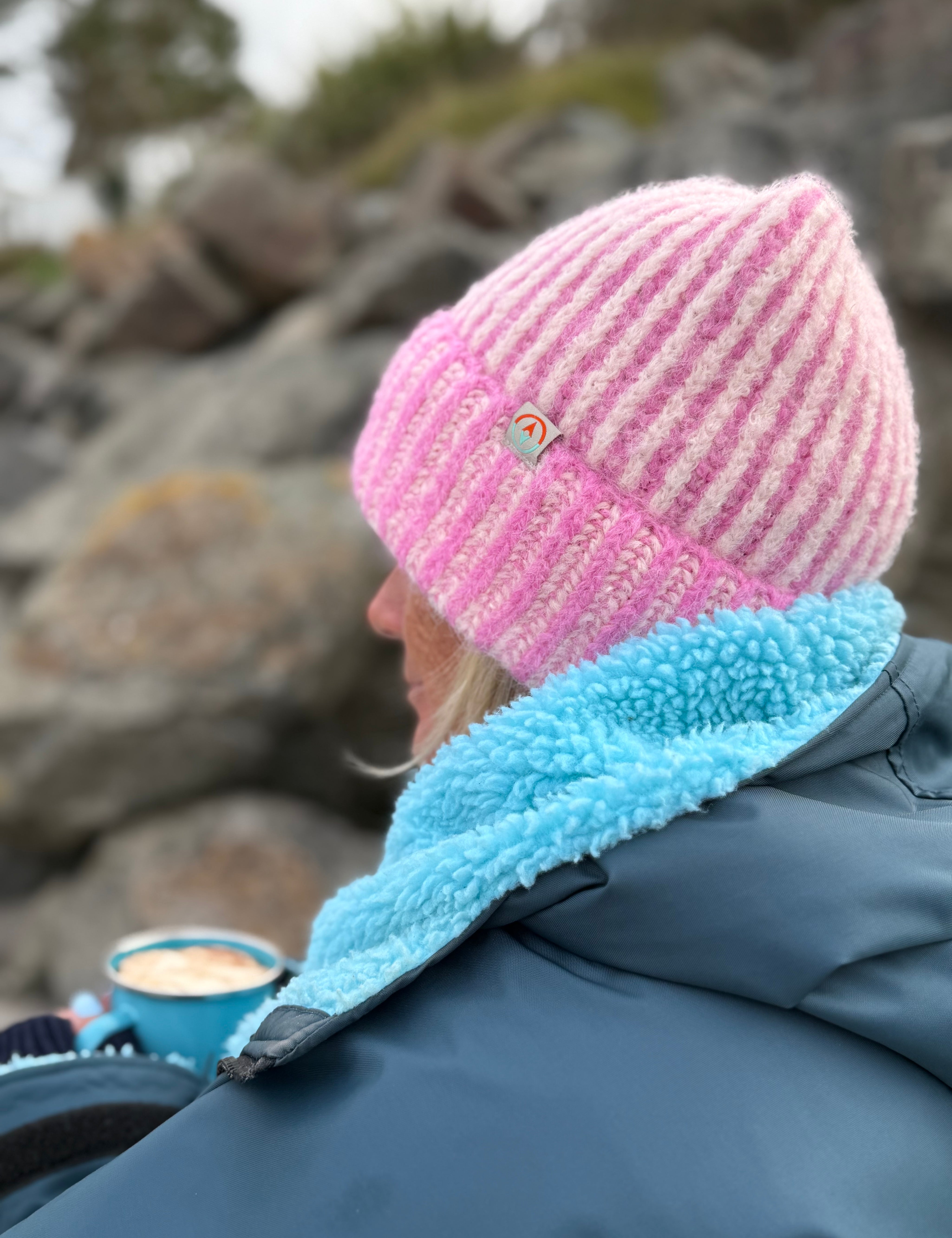 Person wearing a pink and white knit hat with a blue fleece lining, sitting by rocks.