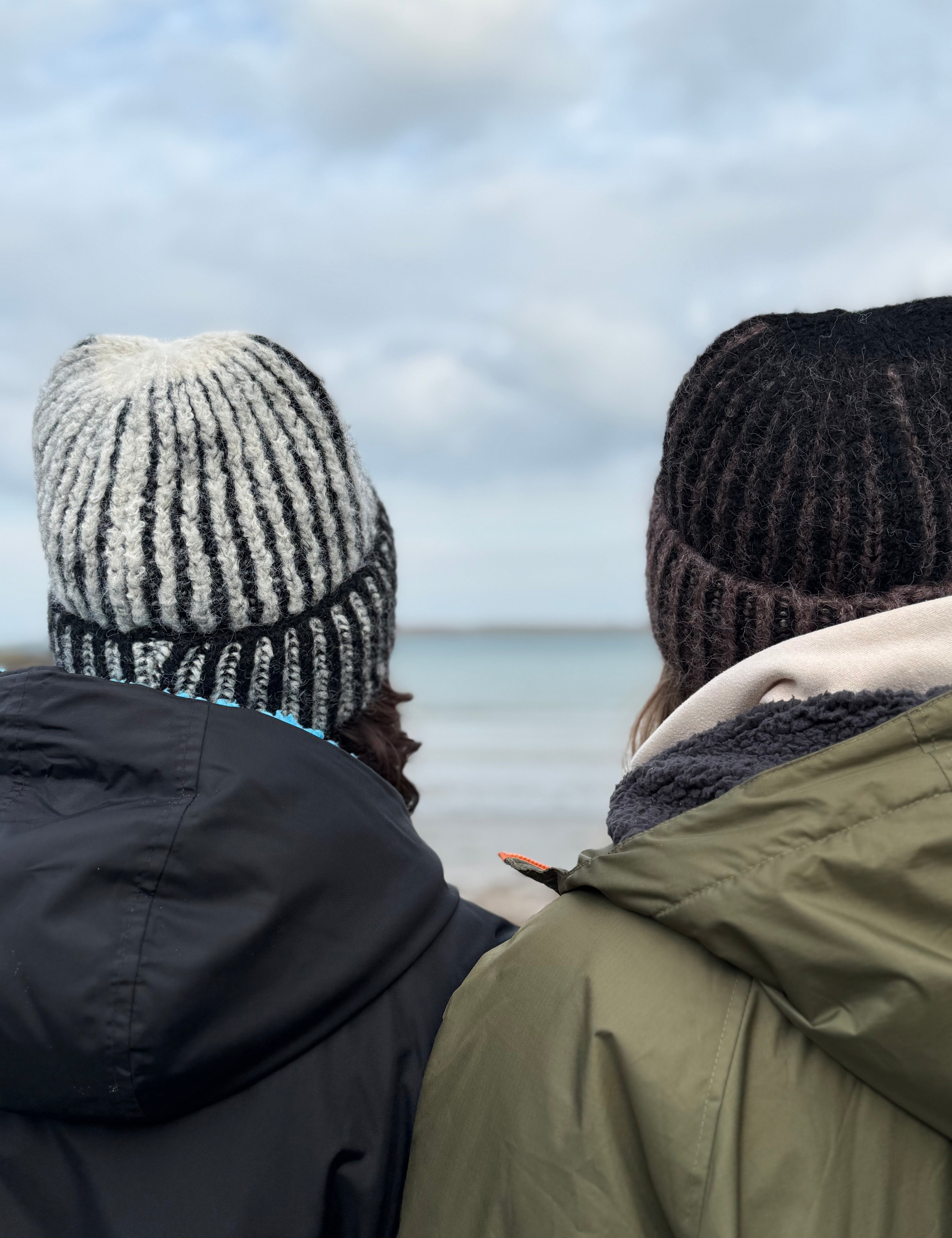 Two people wearing knit hats and winter coats looking out at a body of water.
