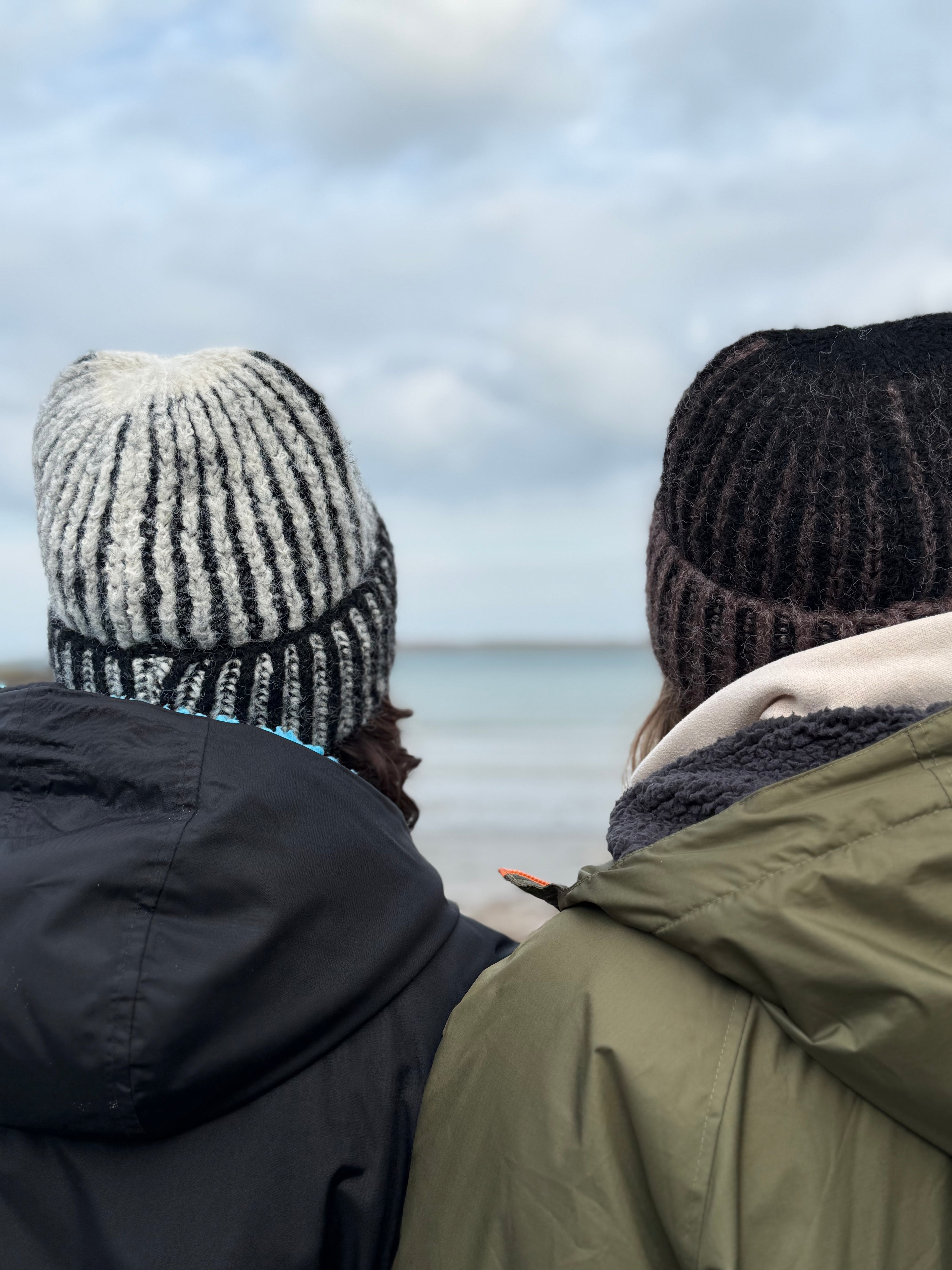Two people wearing knit hats and winter coats looking out at a body of water.