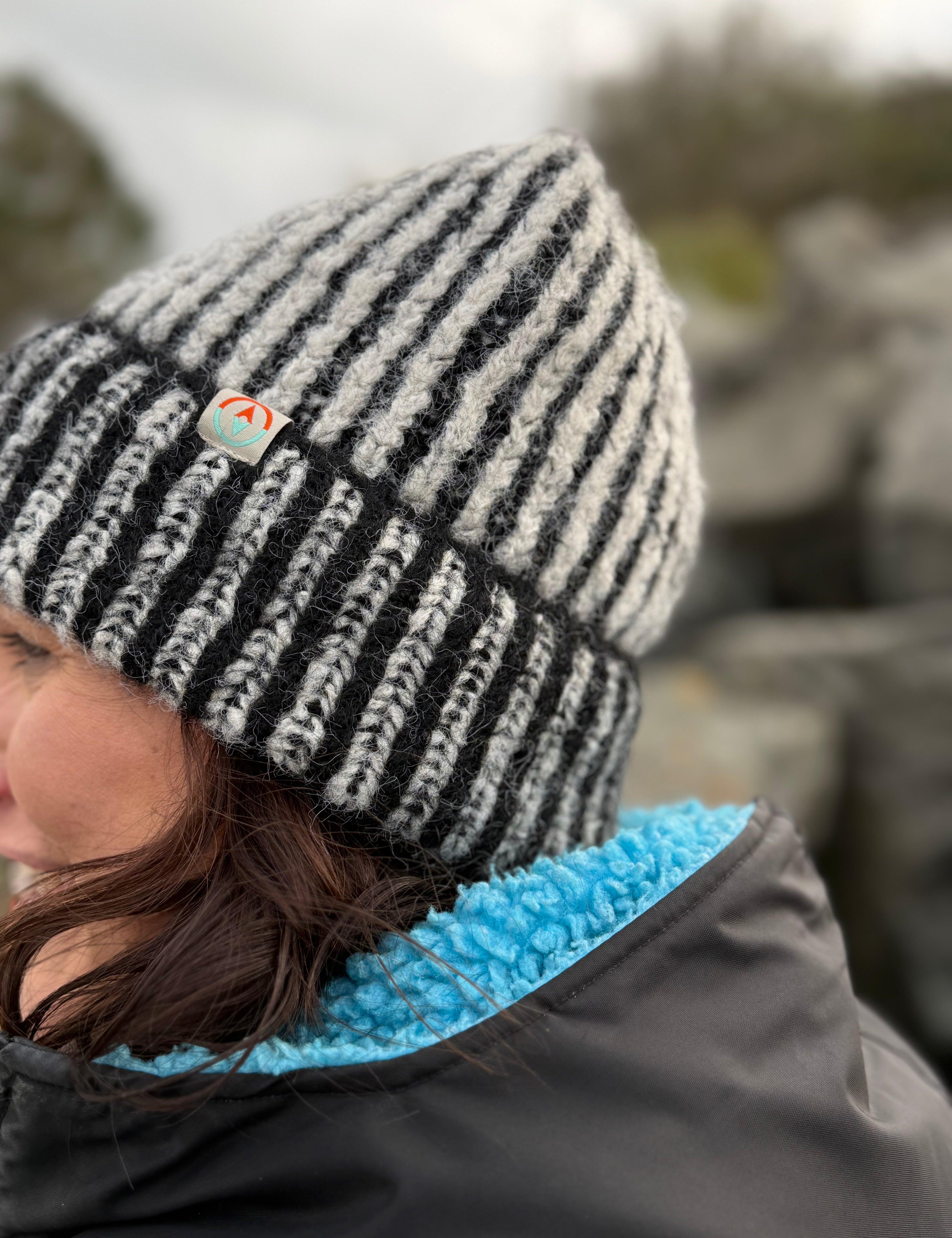 Person wearing a black and white striped beanie with a logo, outdoors.