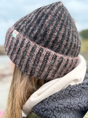 Person wearing a knitted beanie and scarf with a blurred natural background