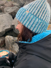 Person wearing a blue and white striped beanie and black jacket on rocky terrain
