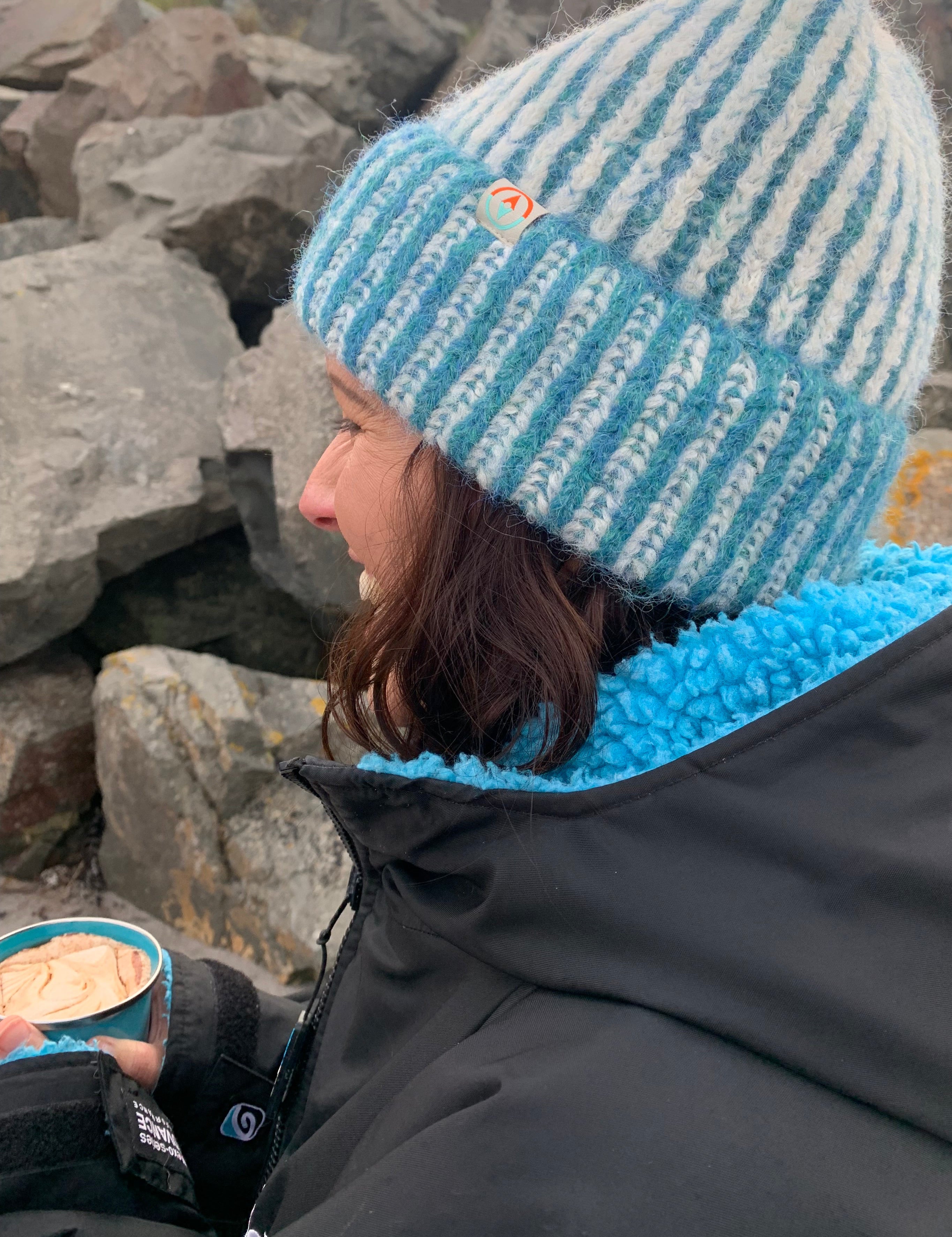 Person wearing a blue and white striped beanie and black jacket on rocky terrain