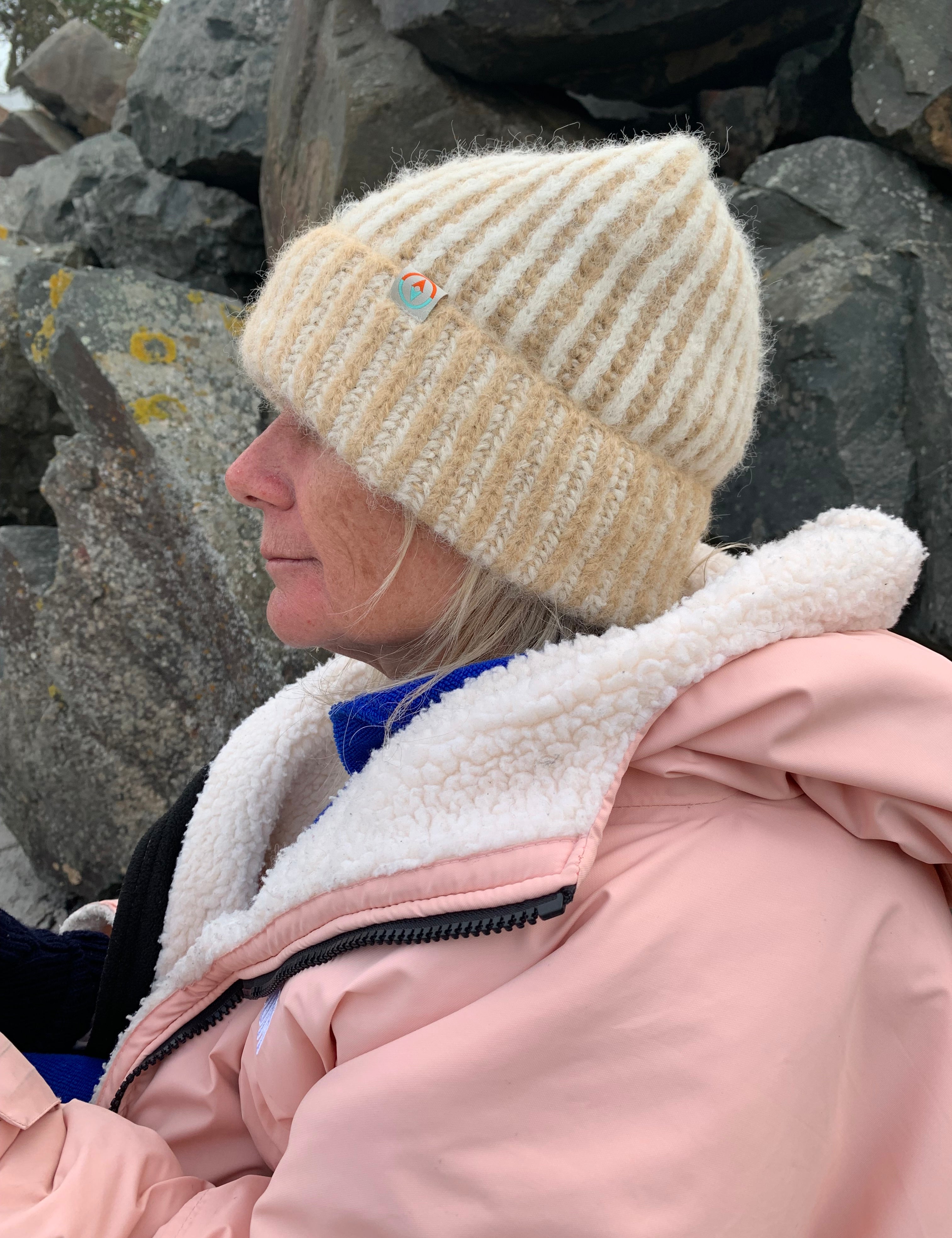 Person wearing a beige knit beanie and pink jacket on a rocky surface