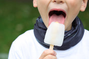 Close up image of a young boy wearing the multiway Infinity Band (snood) around his neck outdoors eating an ice lolly showing its grey and black design inspired by The Giants Causeway in Northern Ireland. 
