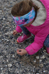 Young girl in a pink coat wearing the Beach Bounty Infinity Band in pinks, blues and navy as she kneels down to collect shells at the beach.