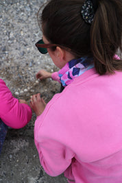 Lady wearing pink sweatshirt and the pink, navy and turquoise blue Infinity Band or snood around her neck while collecting shells at the beach with a young girl in a pink coat.