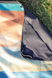 Sustainable waterproof picnic blanket made from recycled polyester, oversized yet packable as it folds flat into a laptop size to slide into a backpack. Zip corner pocket and stake loops and sand pockets to keep it in place. 