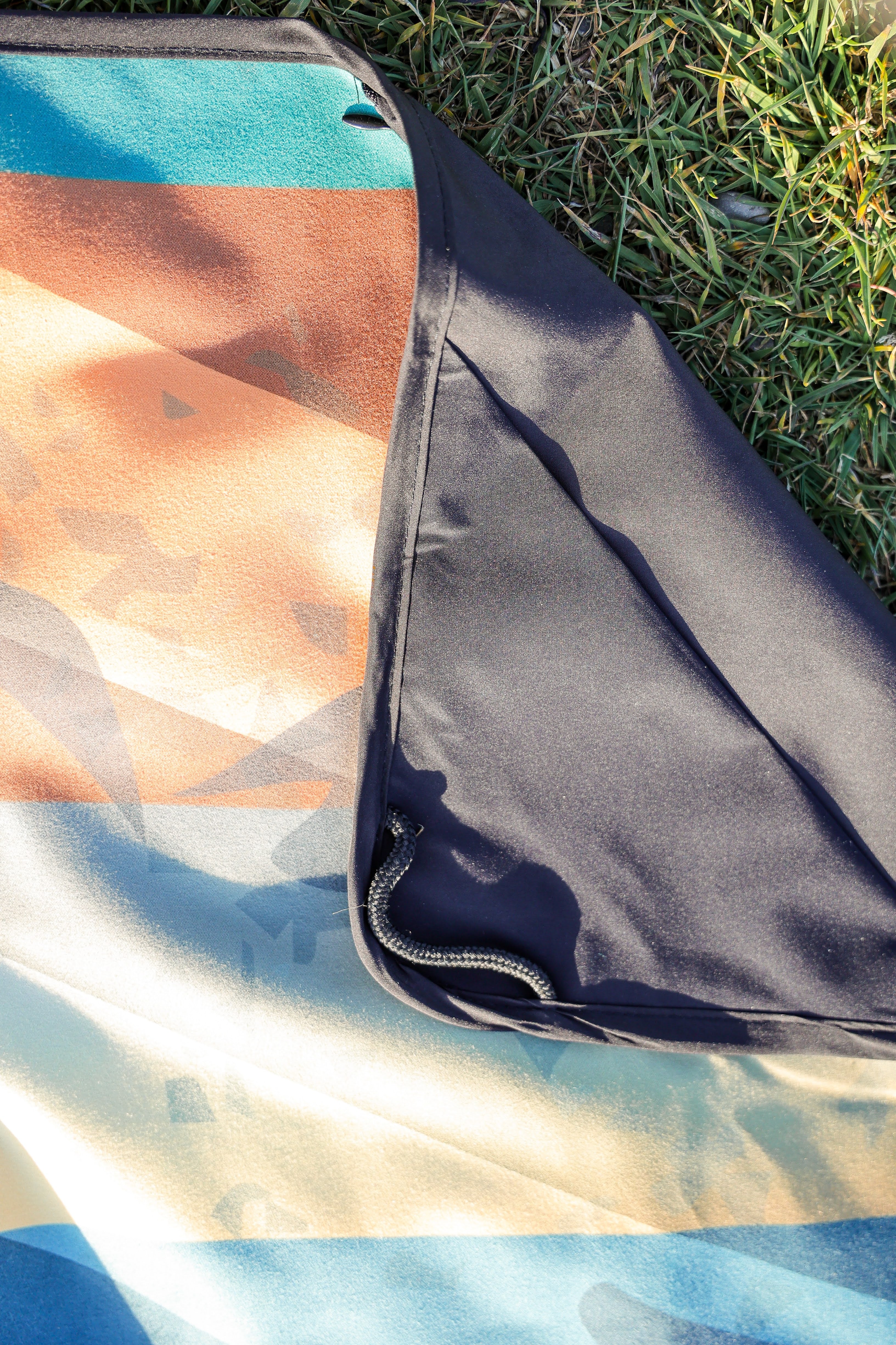 Sustainable waterproof picnic blanket made from recycled polyester, oversized yet packable as it folds flat into a laptop size to slide into a backpack. Zip corner pocket and stake loops and sand pockets to keep it in place. 