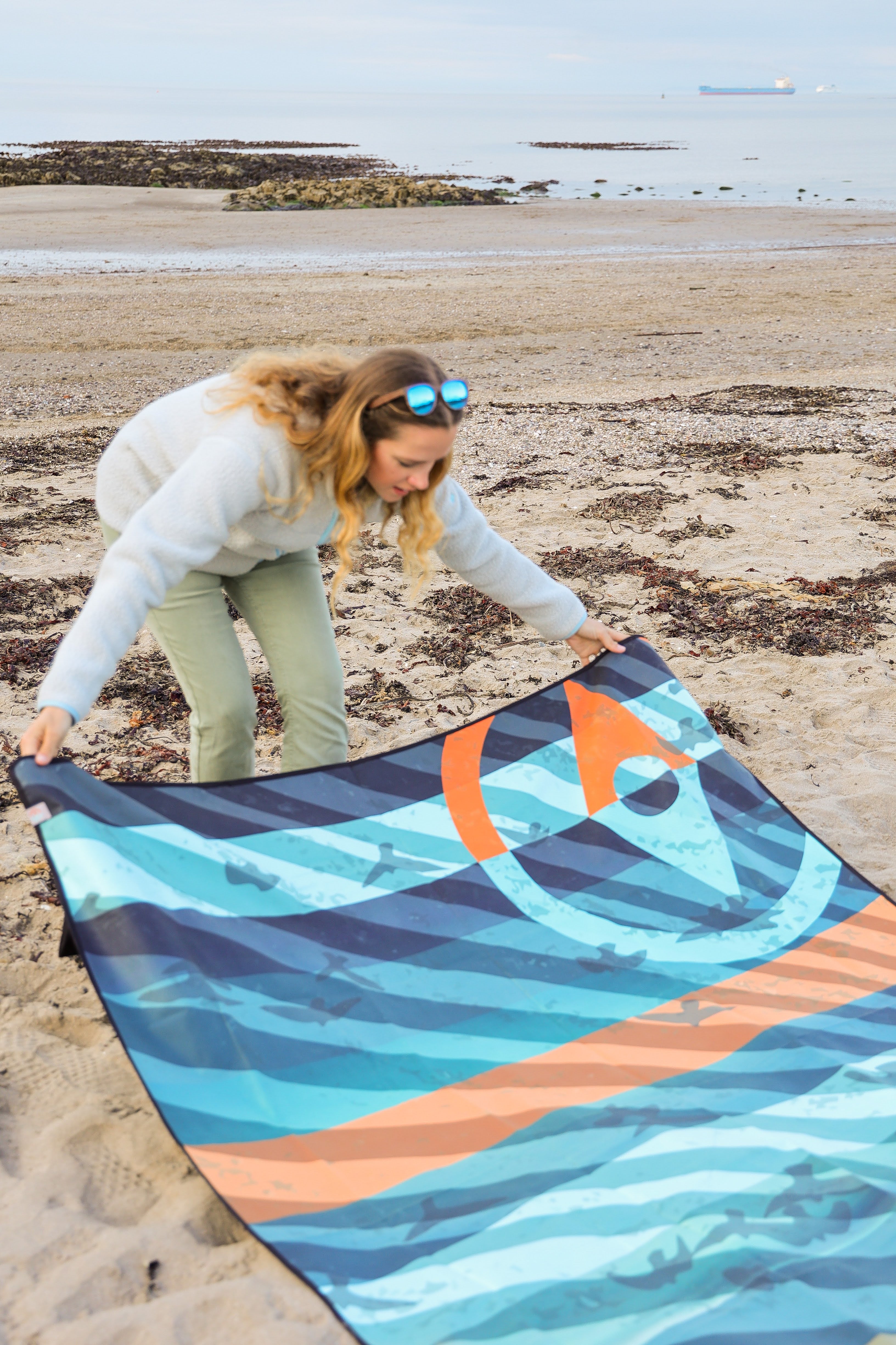 Sustainable waterproof picnic blanket made from recycled polyester, oversized yet packable as it folds flat into a laptop size to slide into a backpack. Zip corner pocket and stake loops and sand pockets to keep it in place. 