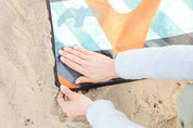 Sustainable waterproof picnic blanket made from recycled polyester, oversized yet packable as it folds flat into a laptop size to slide into a backpack. Zip corner pocket and stake loops and sand pockets to keep it in place. 