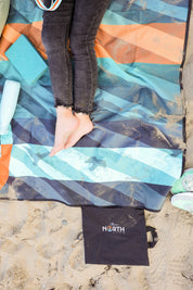 Sustainable waterproof picnic blanket made from recycled polyester, oversized yet packable as it folds flat into a laptop size to slide into a backpack. Zip corner pocket and stake loops and sand pockets to keep it in place. 
