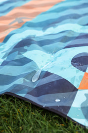 Sustainable waterproof picnic blanket made from recycled polyester, oversized yet packable as it folds flat into a laptop size to slide into a backpack. Zip corner pocket and stake loops and sand pockets to keep it in place. 