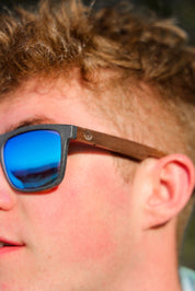 This sustainable rectangular frame is made with a speckled charcoal wheatstraw frame and walnut wood temple and is fitted with UV400 polarised lenses in two colours, smoke and mirrored sky blue. It's lightweight, comfortable and eco-friendly using plastic alternative materials. 