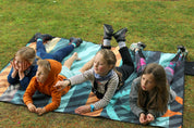 Sustainable waterproof picnic blanket made from recycled polyester, oversized yet packable as it folds flat into a laptop size to slide into a backpack. Zip corner pocket and stake loops and sand pockets to keep it in place. 