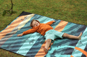 Sustainable waterproof picnic blanket made from recycled polyester, oversized yet packable as it folds flat into a laptop size to slide into a backpack. Zip corner pocket and stake loops and sand pockets to keep it in place. 