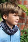 Boy wearing the multiway Infinity Band (snood) around his neck outdoors in a walled garden showing its grey and black design inspired by The Giants Causeway in Northern Ireland. 